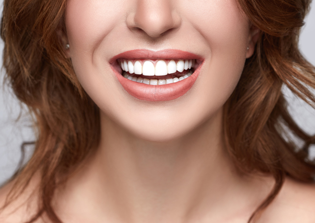 Woman with bright white teeth smiling broadly at camera against neutral background.