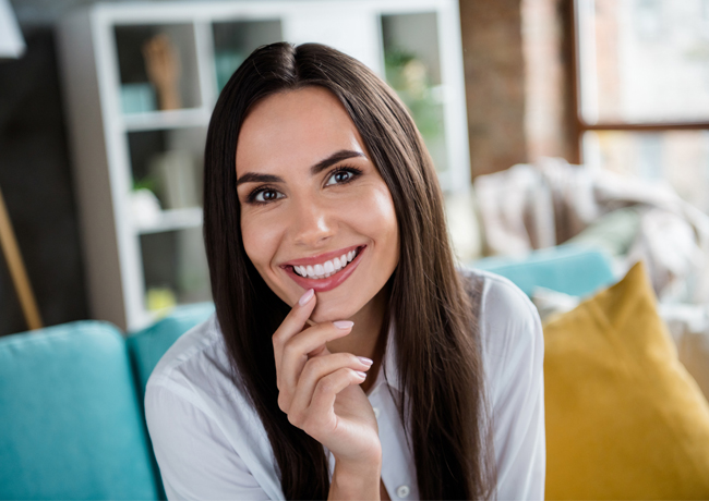 Woman smiling at camera in modern living room with colorful pillows and shelving.