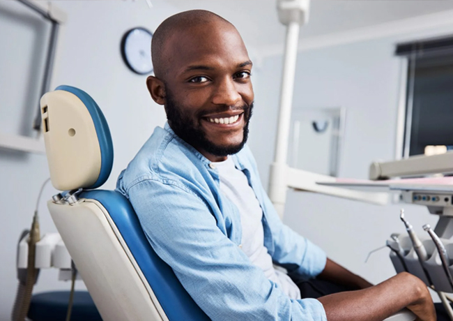 Smiling man in dental chair wearing light blue shirt at modern dental office.