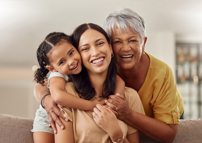 Three generations of women smiling together on a couch in a bright, modern home interior.