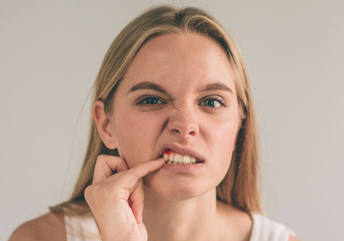 Woman with finger on cheek smiling against neutral background, dental practice portrait.